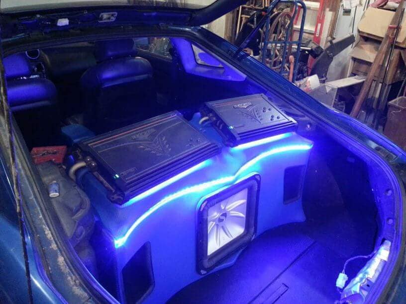 Blue-lit custom subwoofer enclosure installed in a vehicle cargo area